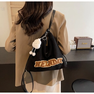 Détail du sac bandoulière en toile noire avec broderie HELNDAY marron et pendentif en peluche