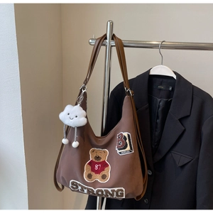 Detail of a brown tote bag featuring bear embroidery and a cloud charm on a hanger