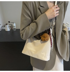 Detalle del bolso bandolera beige media luna con logo dorado y colgante de peluche