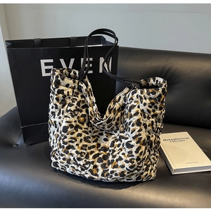 Quilted leopard print tote bag placed on a black leather sofa with a book and shopping bag