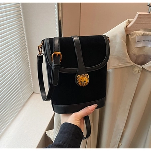 Detail of black suede bucket bag featuring a golden bear emblem and leather strap