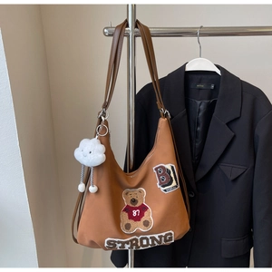 Close-up of brown tote bag featuring teddy bear embroidery and a cloud plush charm