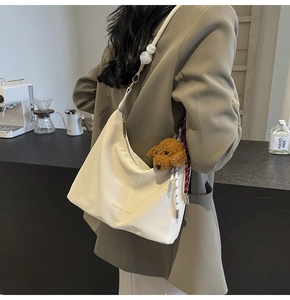 Detalle del bolso de media luna blanco con colgante de oso y cuentas decorativas de mármol