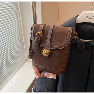 Detail of dark brown bucket bag with gold bear lock and textured matte leather finish