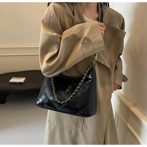 Détail du sac croissant en cuir matelassé noir avec chaîne dorée sur un trench-coat