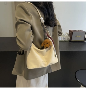 Detalle del bolso hobo blanco crema con correa de perlas y colgante de perro de peluche