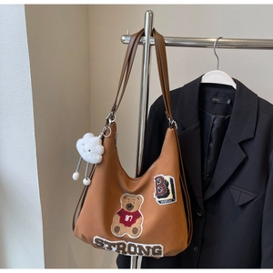 Detail of a brown Hobo tote bag featuring retro bear embroidery and a plush cloud charm