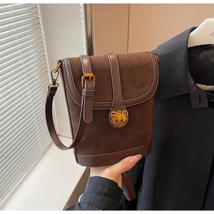 Detailed close-up of brown suede bucket bag featuring a gold bear metal clasp and leather strap