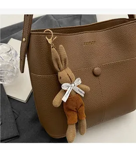 Detail view of brown lychee grain leather bucket bag with a cute knit rabbit charm