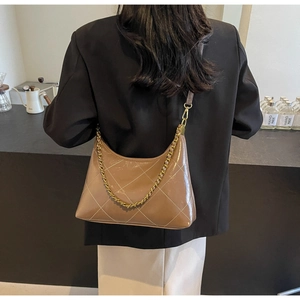 Détail d'un sac en cuir matelassé marron avec chaîne dorée sur un blazer noir