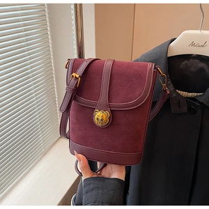 Detail of burgundy bucket bag featuring suede leather mix and gold bear ornament