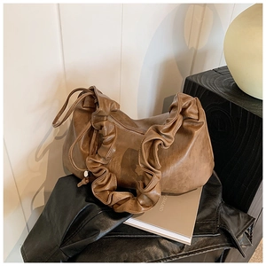 Détail d'un sac à main plissé marron sur une veste en cuir et des livres vintage