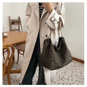 Detail of large leopard print tote bag with metal chain strap on model in trench coat