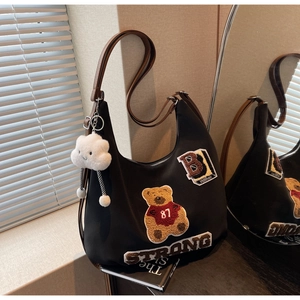 Detail of black hobo bag featuring teddy bear patches and a white cloud charm accessory