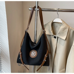 Détails macro du sac cabas avec logo M, bandoulières en cuir et accents de chaîne