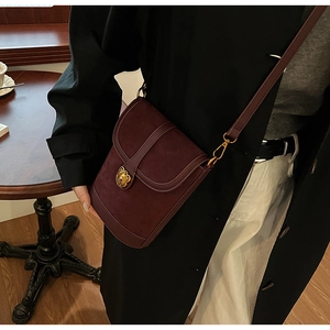 Detail of burgundy crossbody bag with golden lion buckle and textured suede fabric