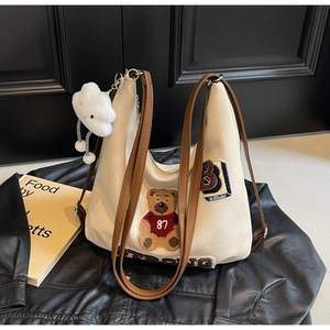 Detail of canvas tote bag with bear patch embroidery and cloud plush charm on a jacket
