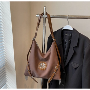 Détail du grand sac cabas marron foncé avec logo M en métal et chaînes sur un blazer