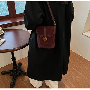Detail view of burgundy bucket bag with golden bear lock on a cafe table background