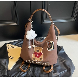 Detail of brown tote bag featuring bear embroidery patch and plush cloud charm accessory