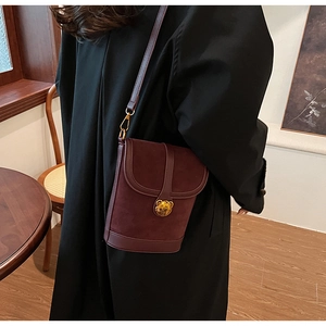 Detail of burgundy suede mini bucket bag with a golden bear metal clasp on model