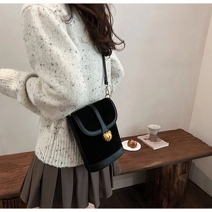 Detail of a black velvet crossbody bag featuring a 3D golden bear buckle on a model