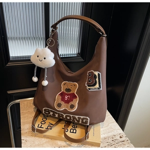 Close-up of brown tote bag with 87 bear patch, B letter and cloud plush charm
