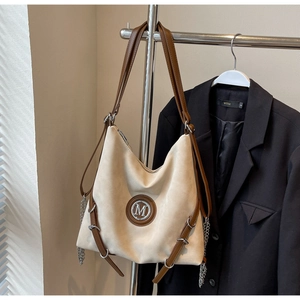 Détail d'un grand sac cabas en daim beige avec un logo M métallique sur le devant