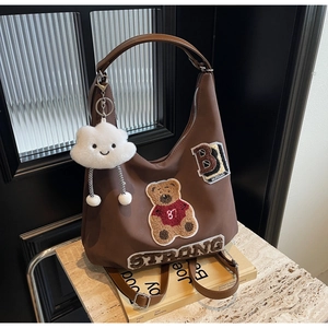 Detail of brown faux leather crescent bag with bear patch and plush cloud charm