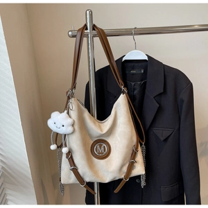 Dettaglio della borsa tote crema con logo M, tracolla in pelle e ciondolo a nuvola bianca