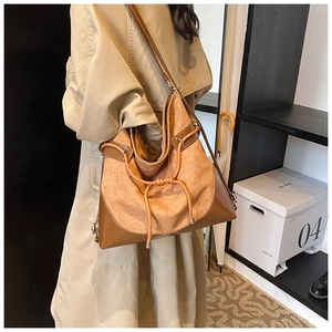 Close-up of a large tan suede shoulder bag with drawstring detail on a beige trench coat