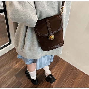 Detail of dark brown suede bucket bag with gold bear buckle and leather patchwork design