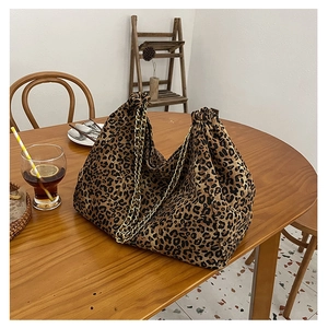 Detail of leopard print tote bag with gold chain strap and drawstring closure on wooden table