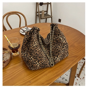 Detail view of large leopard print tote bag with gold chain strap on a wooden table