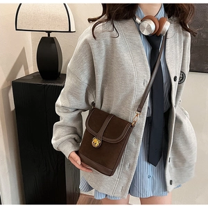 Detail of a brown suede crossbody bag featuring a golden bear charm and adjustable strap