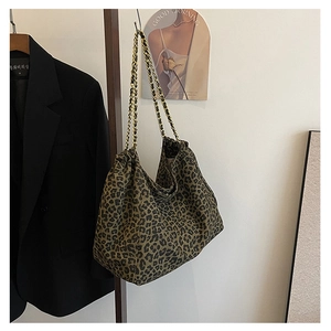 Detail of leopard print tote bag with golden chain straps against minimalist background
