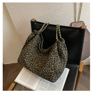 Detail of leopard print tote bag featuring gold chain strap on a leather chair background