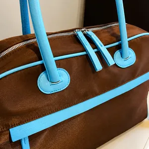 Details blauer Ledergriffe und Reißverschlüsse an einer braunen Nylon Reisetasche