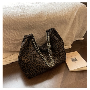 Detail of leopard print tote bag with gold chain straps and drawstring closure on wood floor