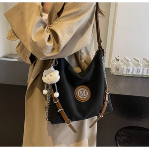 Dettaglio borsa tote in nylon nero con cinturini in pelle marrone e ciondolo a nuvola