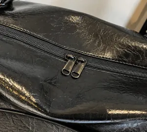 Close-up of dual metal zippers on black travel bag with premium wrinkled leather texture