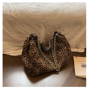 Detail of leopard print tote bag with gold chain strap on soft fabric background