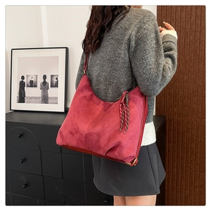 Detail of dark red suede shoulder bag with woven pendant showing large capacity and texture