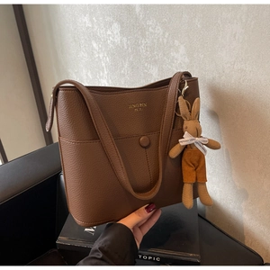 Close-up of brown litchi pattern leather bucket bag with a cute plush rabbit charm