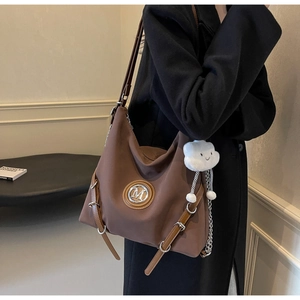Détail d'un sac cabas marron avec logo M métallique et breloque peluche nuage blanc