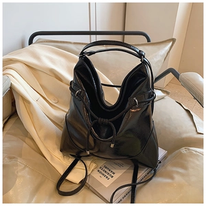 Detail of a black patent leather bucket bag with silver hardware on a beige chair