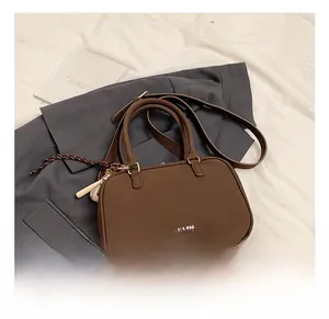 Dettaglio della borsa a bauletto marrone scuro con doppi manici e ciondolo intrecciato