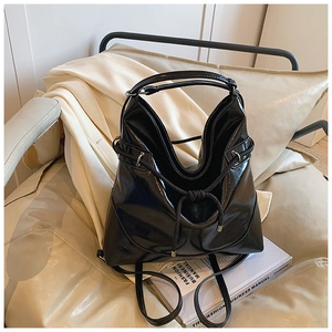 Detail of a black glossy bucket backpack with drawstring closure on a beige sofa
