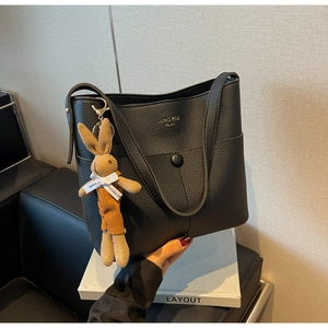 Detail of black lychee grain leather bucket bag with cute brown knit rabbit charm