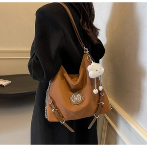 Vista laterale di una borsa tote in pelle marrone con logo M, catena e ciondolo morbido